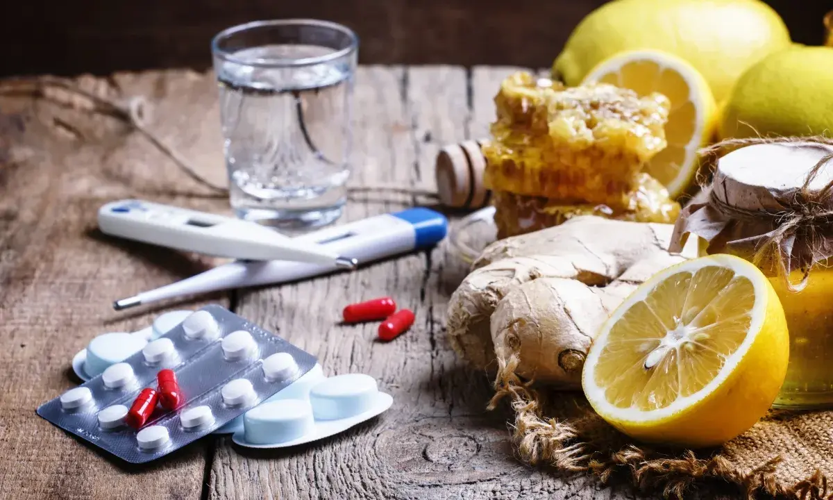 Rimedi naturali e antibiotico umano per canarini: limoni, zenzero, miele, termometro e pillole su un tavolo di legno.