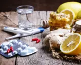 Rimedi naturali e antibiotico umano per canarini: limoni, zenzero, miele, termometro e pillole su un tavolo di legno.