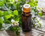Flacone di olio di origano su legno rustico, circondato da rametti fioriti. Utile contro i parassiti.