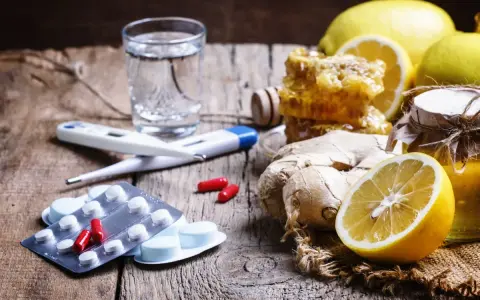 Rimedi naturali e antibiotico umano per canarini: limoni, zenzero, miele, termometro e pillole su un tavolo di legno.
