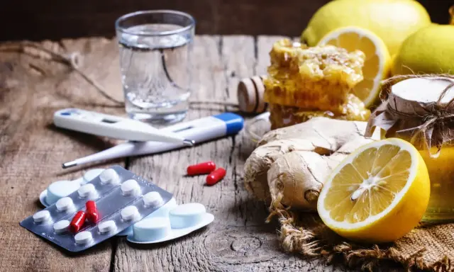 Rimedi naturali e antibiotico umano per canarini: limoni, zenzero, miele, termometro e pillole su un tavolo di legno.